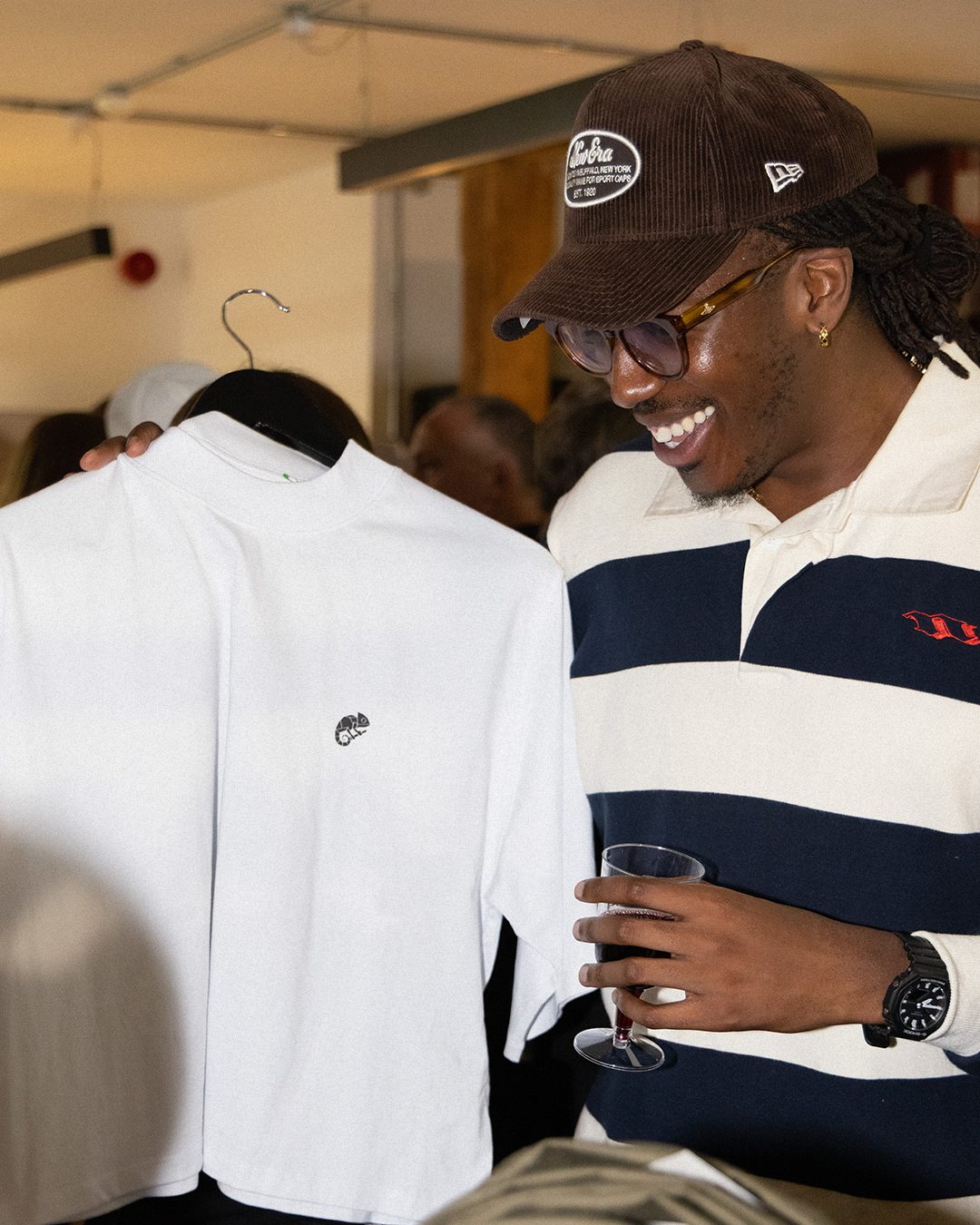A guest smiling as he holds up a white Limits Are Fiction tee with the chameleon logo